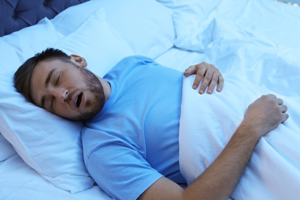 A young man snoring while sleeping in bed at night