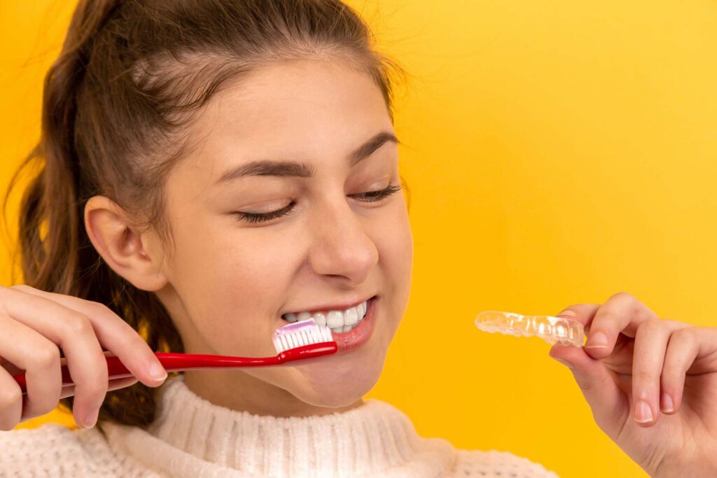 A girl brushing her teeth and holding aligners