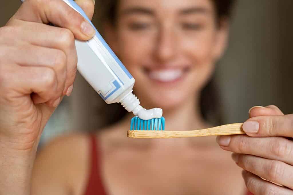 Close up of woman with tooth brush applying paste in bathroom. Closeup of girl hands squeezing toothpaste on ecological wooden brush. Smiling beautiful woman applying toothpaste on eco friendly toothbrush.