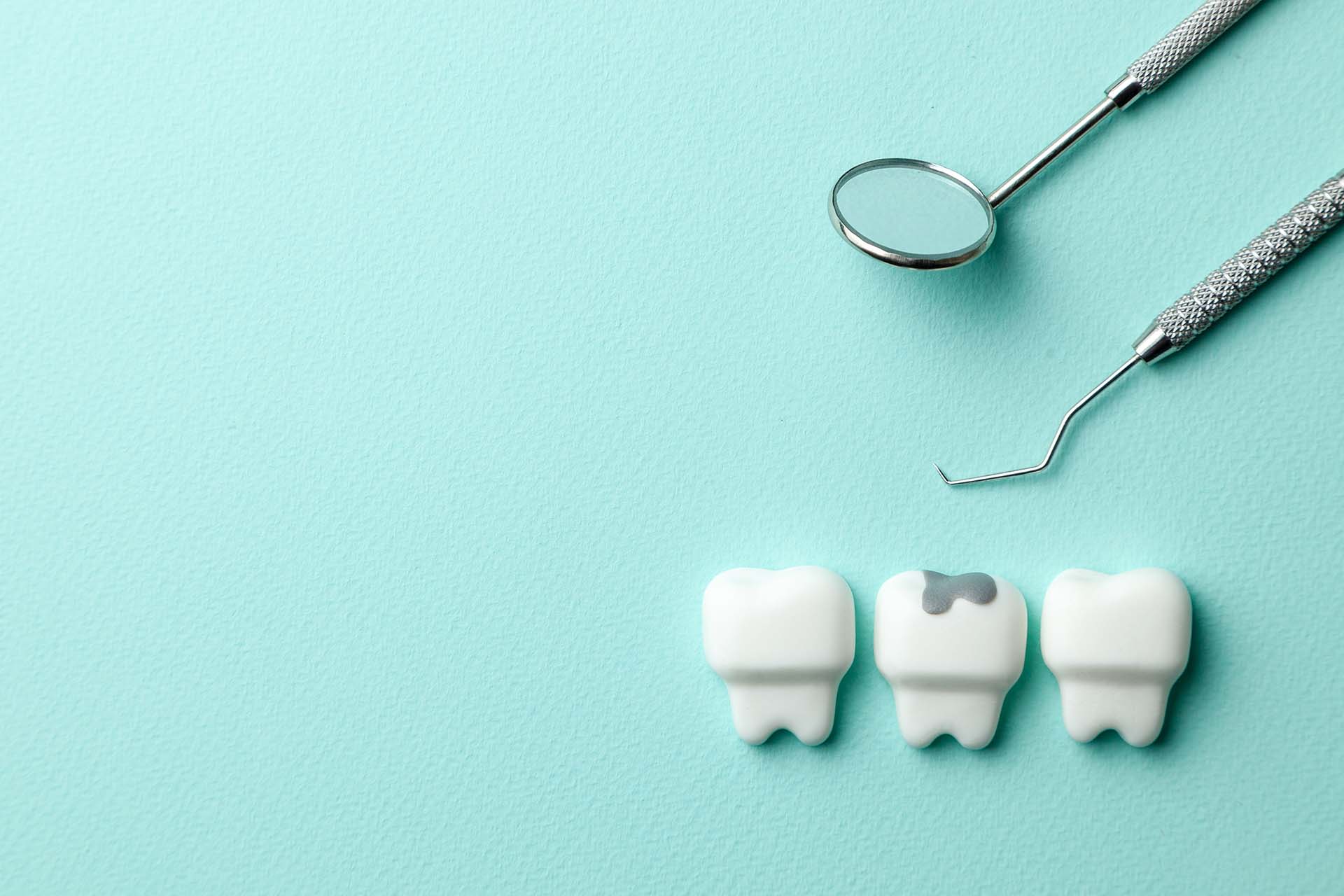 Healthy white teeth and tooth with caries on green mint background and dentist tools mirror, hook. Copy space for text