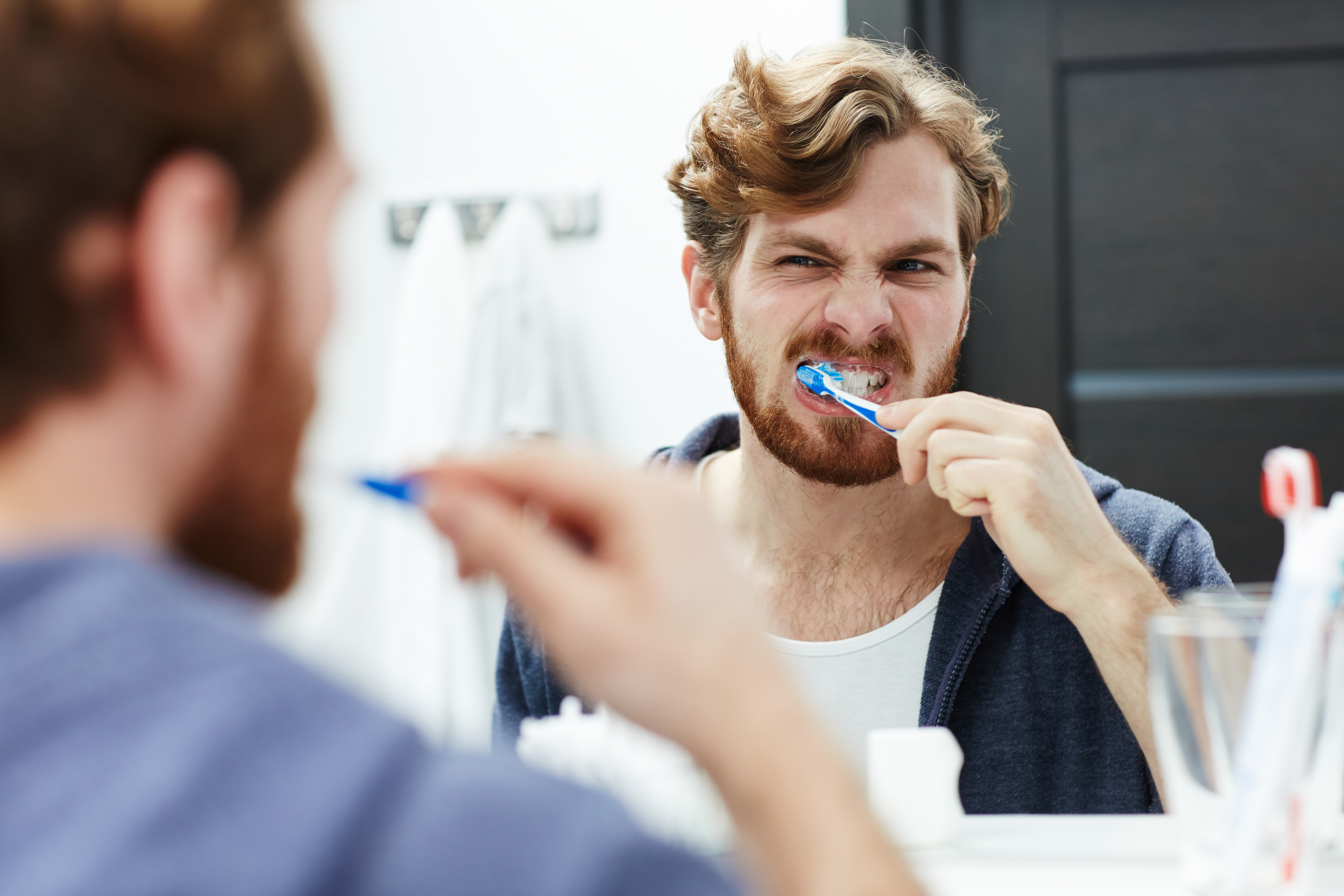 Man brushing his teeth in the bathroom, illustrating daily oral hygiene habits