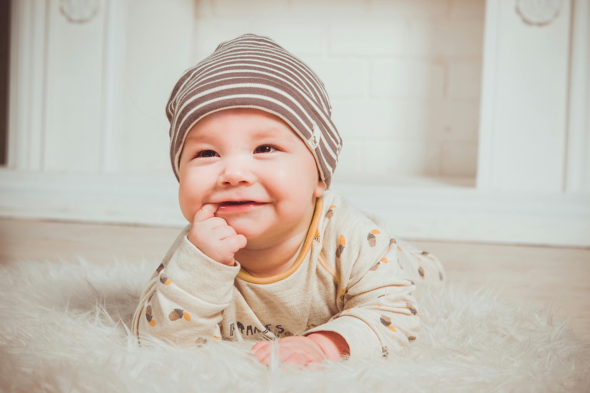 A smiling baby lying on a fluffy rug with a finger in their mouth, illustrating early oral development.