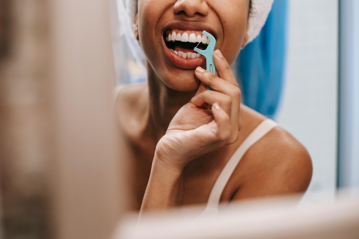 Woman flossing teeth in mirror as part of a periodontal maintenance routine at Aspire Dental Wellness in Charlotte, NC