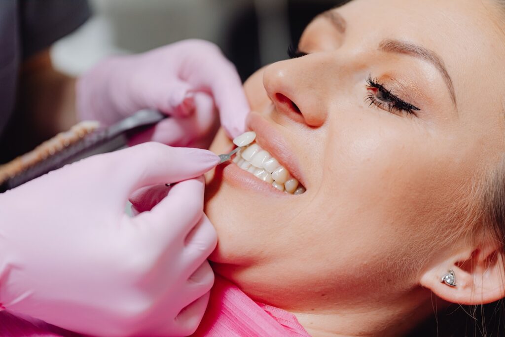 Dentist test-fitting a porcelain veneer onto a patient's front tooth with dental instruments