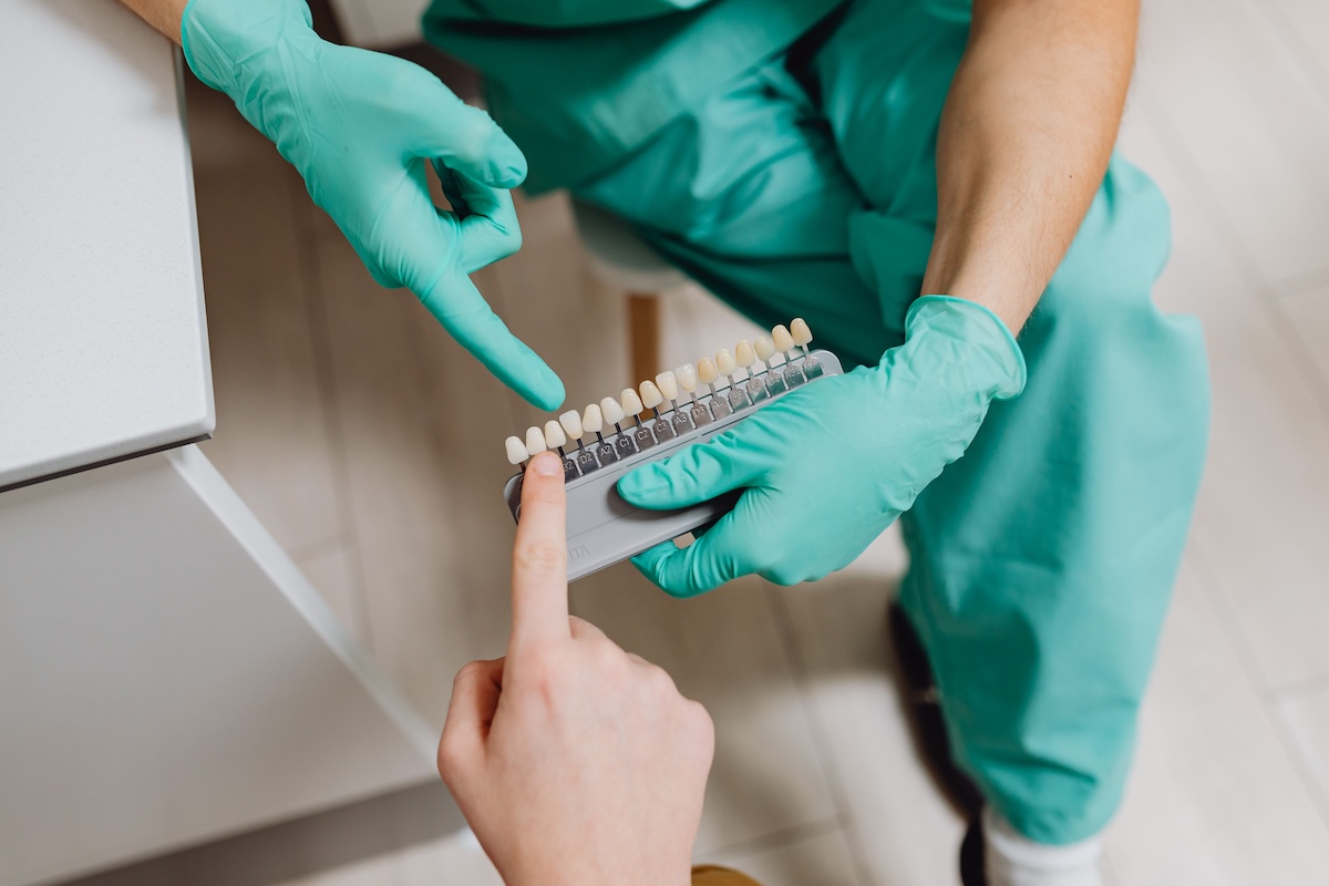 Patient pointing to a shade on a VITA dental shade guide while a dentist selects the tooth color for composite veneers