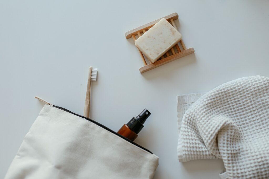 Bamboo toothbrush, travel toiletry bag, spray bottle, soap bar, and folded towel laid out on a white surface