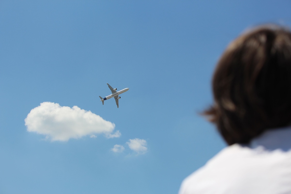 Person watching an airplane in flight, considering travel with a toothache