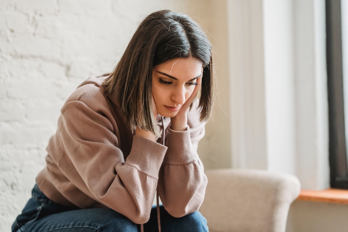Woman sitting on a couch at home holding her chin, looking worried about tooth pain before a trip
