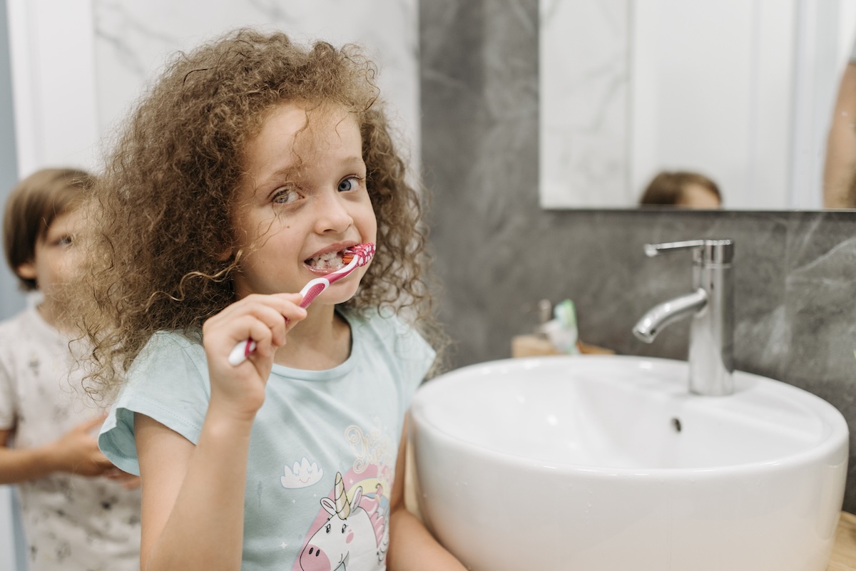 Smiling girl with curly hair brushing her teeth at a bathroom sink as part of a daily routine for healthy gums