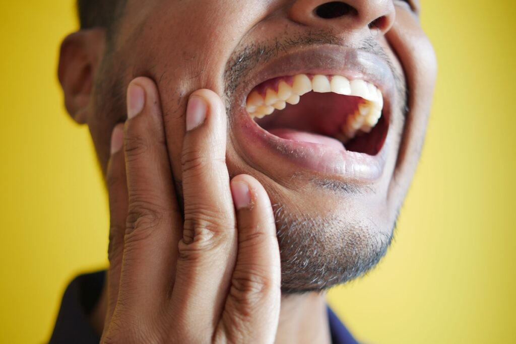 Close-up of a man holding his hand against his cheek near the jaw joint with his mouth open