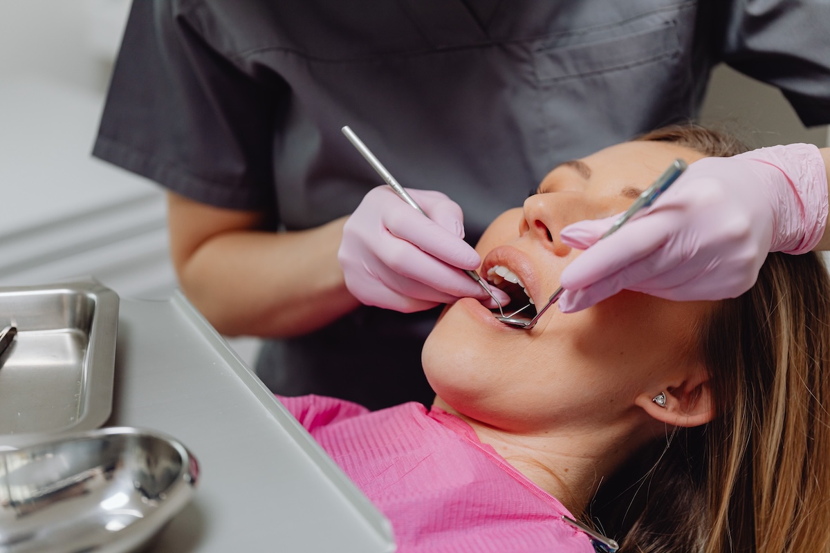 Dental professional in pink gloves checking a patient’s teeth with a mouth mirror during an exam