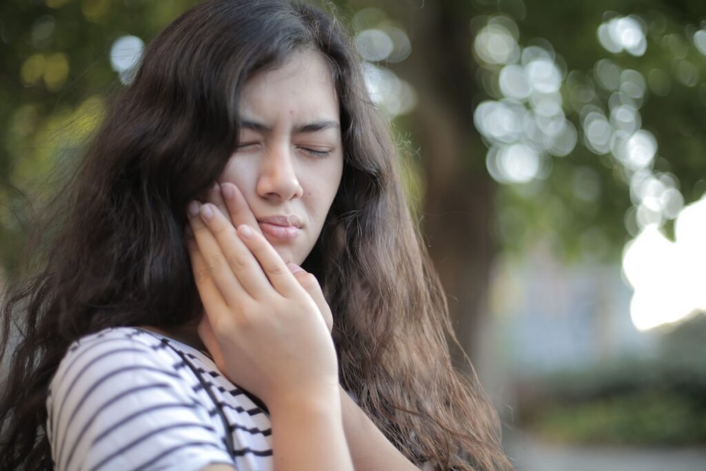 Woman with closed eyes wincing in pain while holding the side of her jaw and cheek