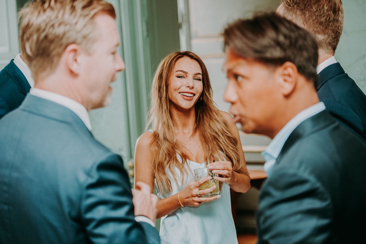 Smiling woman holding a drink while talking with men in suits at a networking event